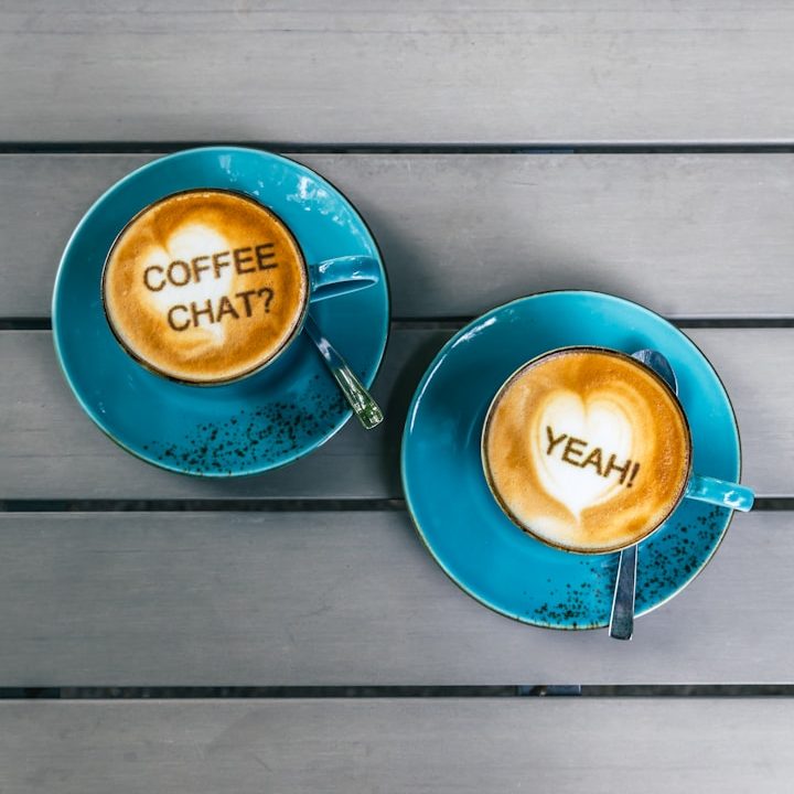 Zwei türkise Cappuccino Tassen, in der linken steht im Schaum "Coffee chat" in der rechten "Yeah"